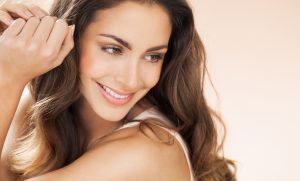 Happy beautiful young woman with long hair smiling over beige background. Fashion and beauty concept in studio.