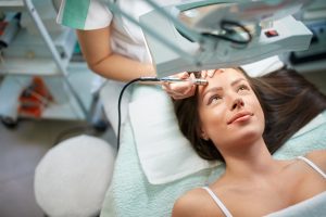 Skillful cosmetologist is undergoing microdermabrasion of skin on female face