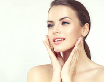 Young, blue eyed pretty woman with sensual smile on the face and delicate, neat make up is touching softly skin of cheeks