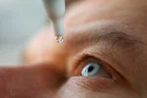 man drops eye drops into his right eye