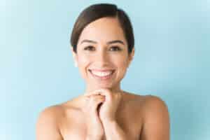 brunette female smile with her hands below her chin against a light blue background