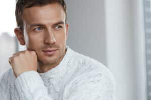 light haired man with blue eyes in a white sweater looking off into the distance. strong jawline and cheekbones
