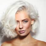 A young woman with a gray bob hair style and dark makeup smirks coyly