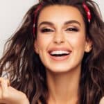 A brunette woman wearing a hairband with a bright smile